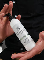 Person holding a white shampoo bottle labeled 'Barbaro' with a black pump.