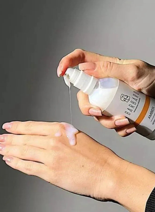 Hand applying a white cream from a Barbaro bottle on a gray background