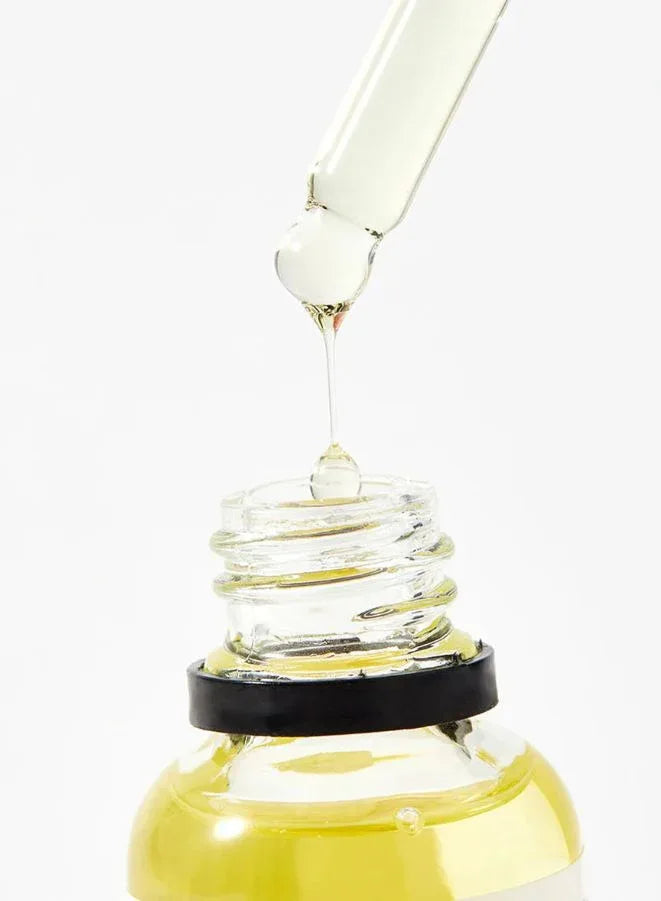Glass dropper with yellow liquid being dripped into a glass container on a white background
