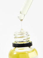 Glass dropper with yellow liquid being dripped into a glass container on a white background