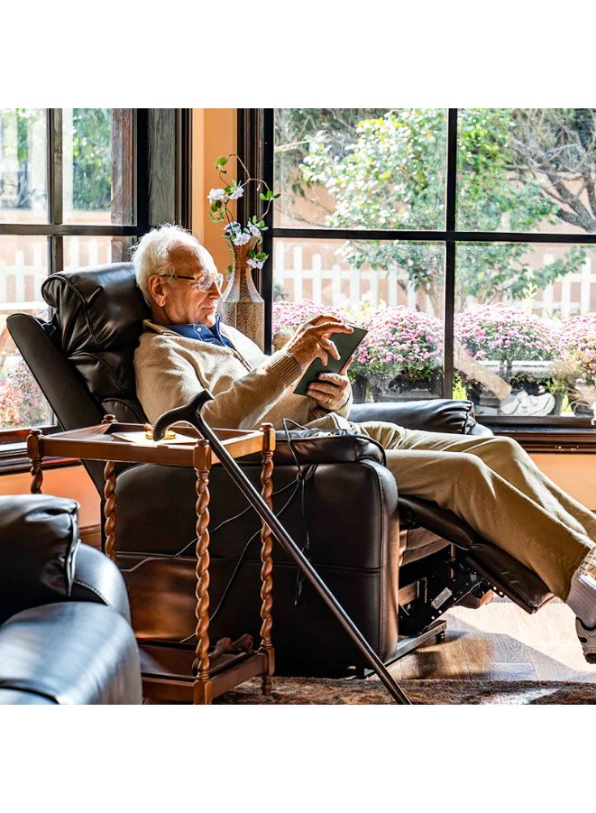 Man sitting in a recliner chair holding a tablet, with a cane beside him, in a room with large windows.